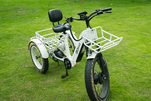 White electric cargo tricycle with front and rear baskets and a backrest, parked on grass.